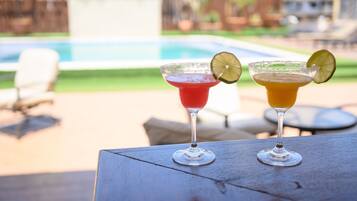 Dos bebidas sobre una mesa, con una piscina al fondo.