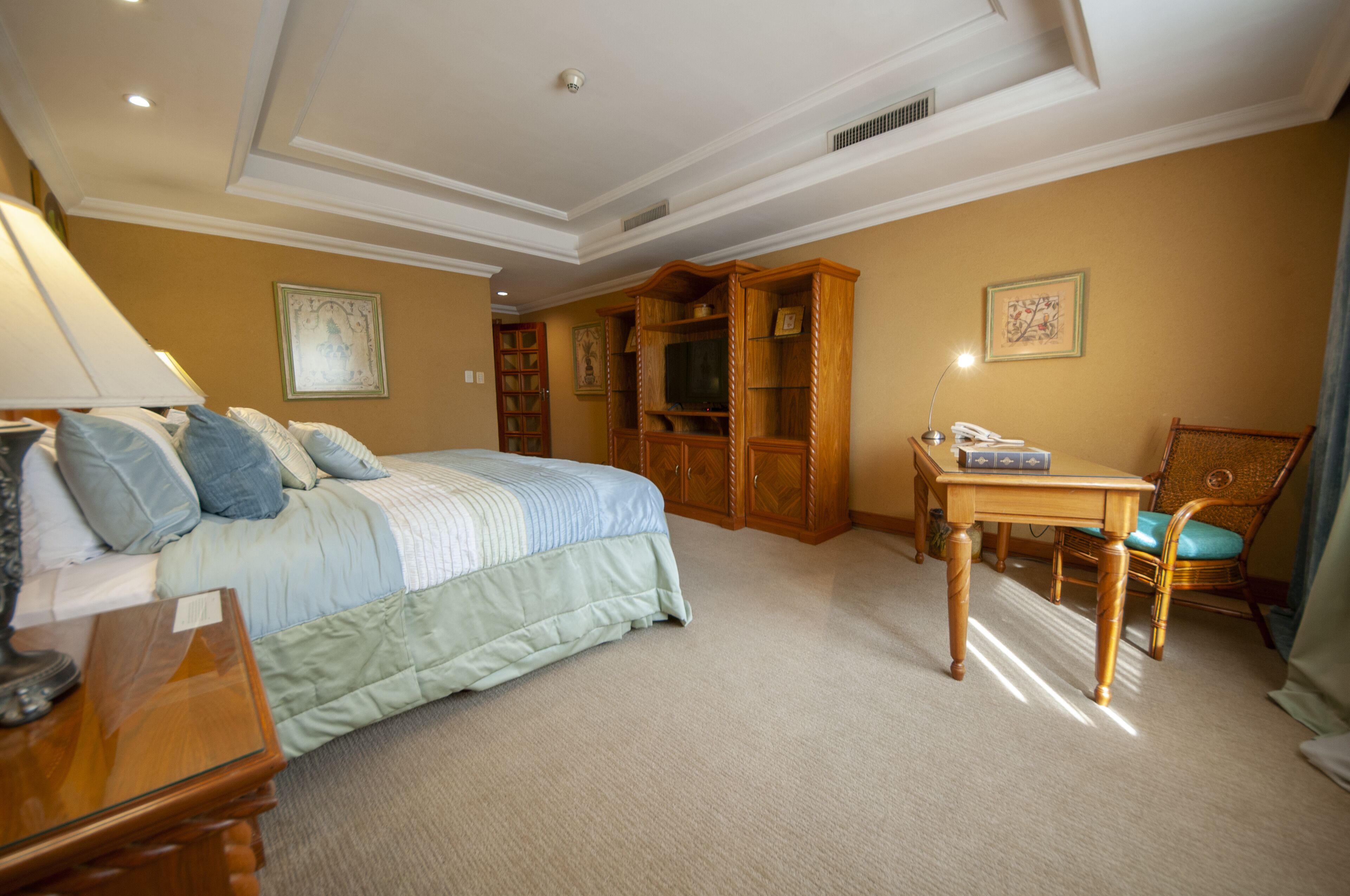 Un dormitorio con una cama, un escritorio y una silla. Hay una estantería y una puerta que da a otra habitación.