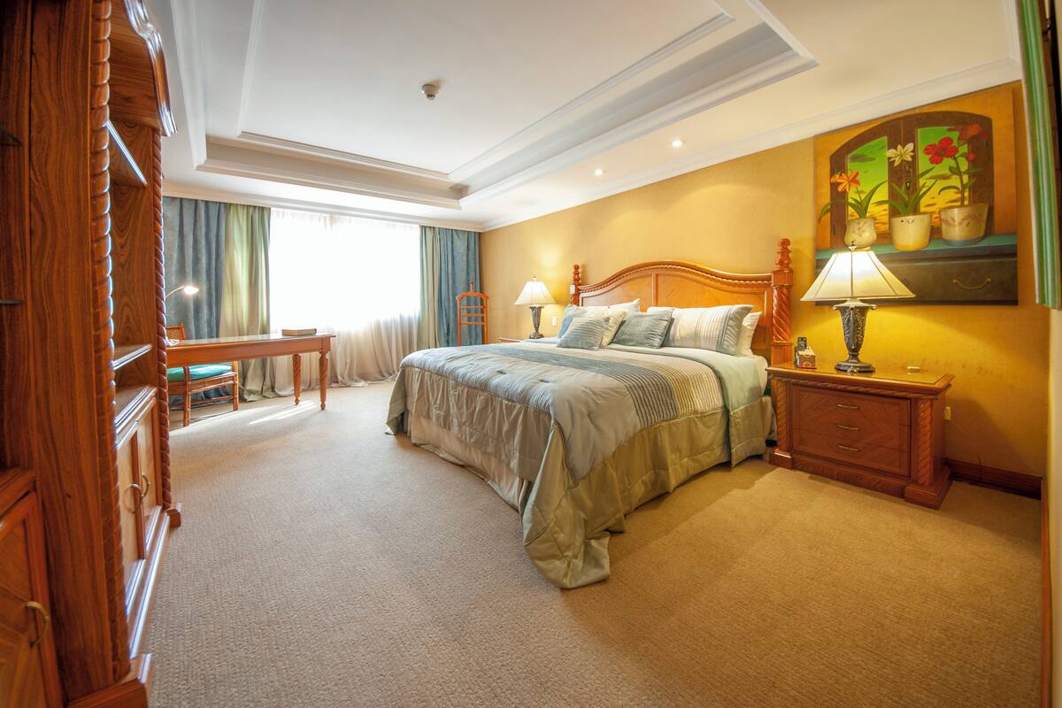 A hotel room with a large bed, a wooden nightstand, a desk, and a chair.