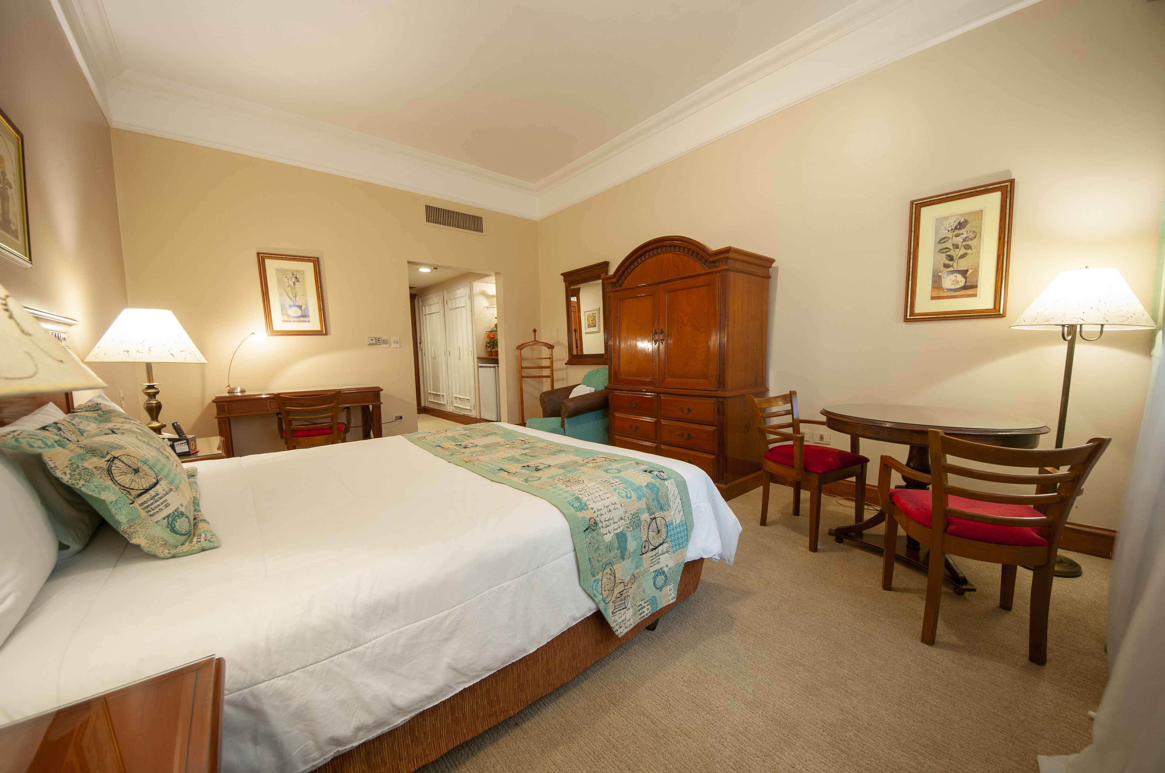A hotel room with a bed, a desk, a chair, a wardrobe, and a lamp.
