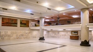 Un vestíbulo amplio con suelo de mármol, columnas imponentes y obras de arte en las paredes.