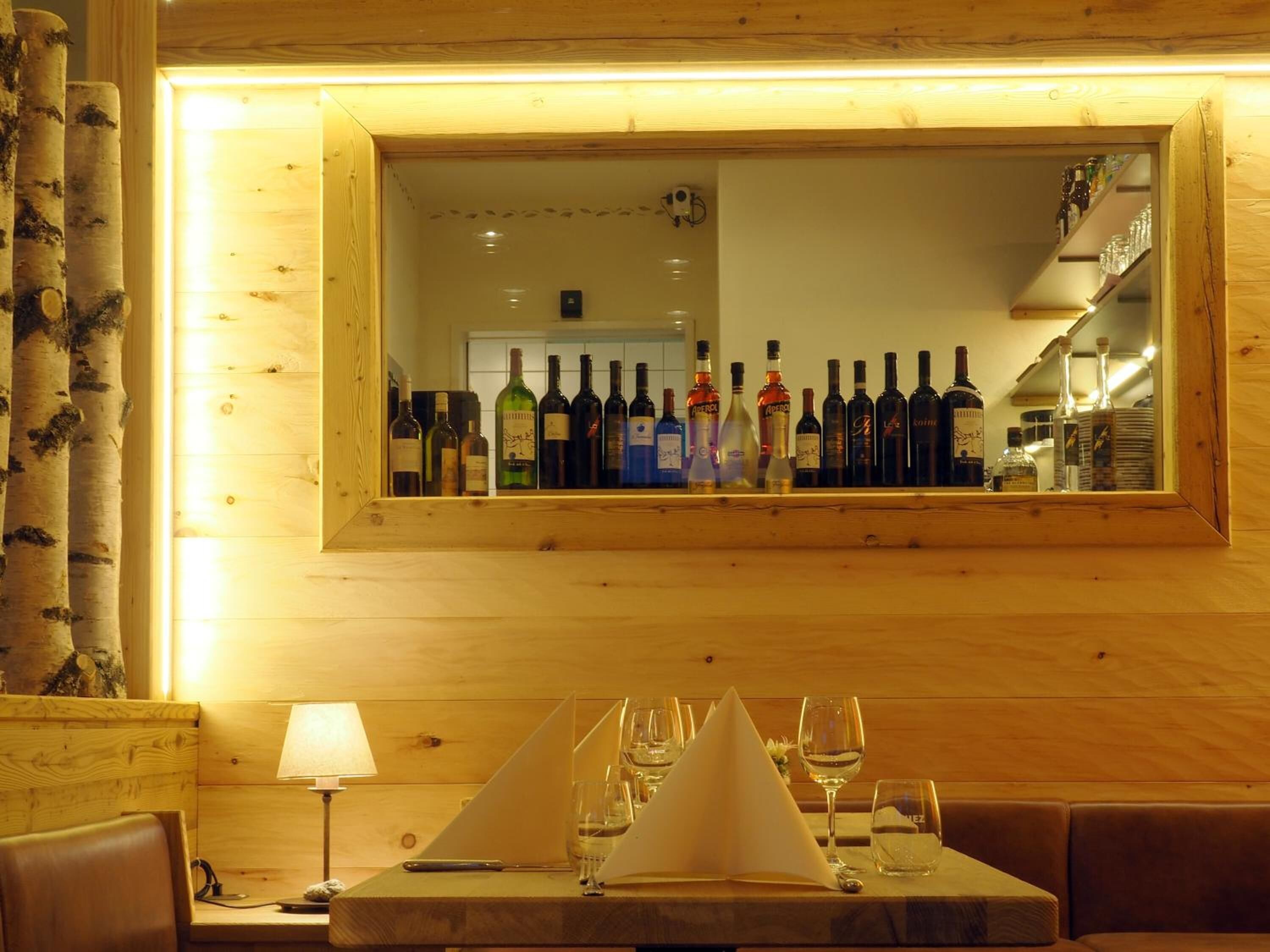 A wooden interior with a bar area, a table set with glasses and a menu, and a mirror reflecting the bar.
