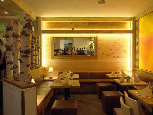 Un restaurante acogedor con paredes de madera, columnas de abedul y una zona de bar con botellas.