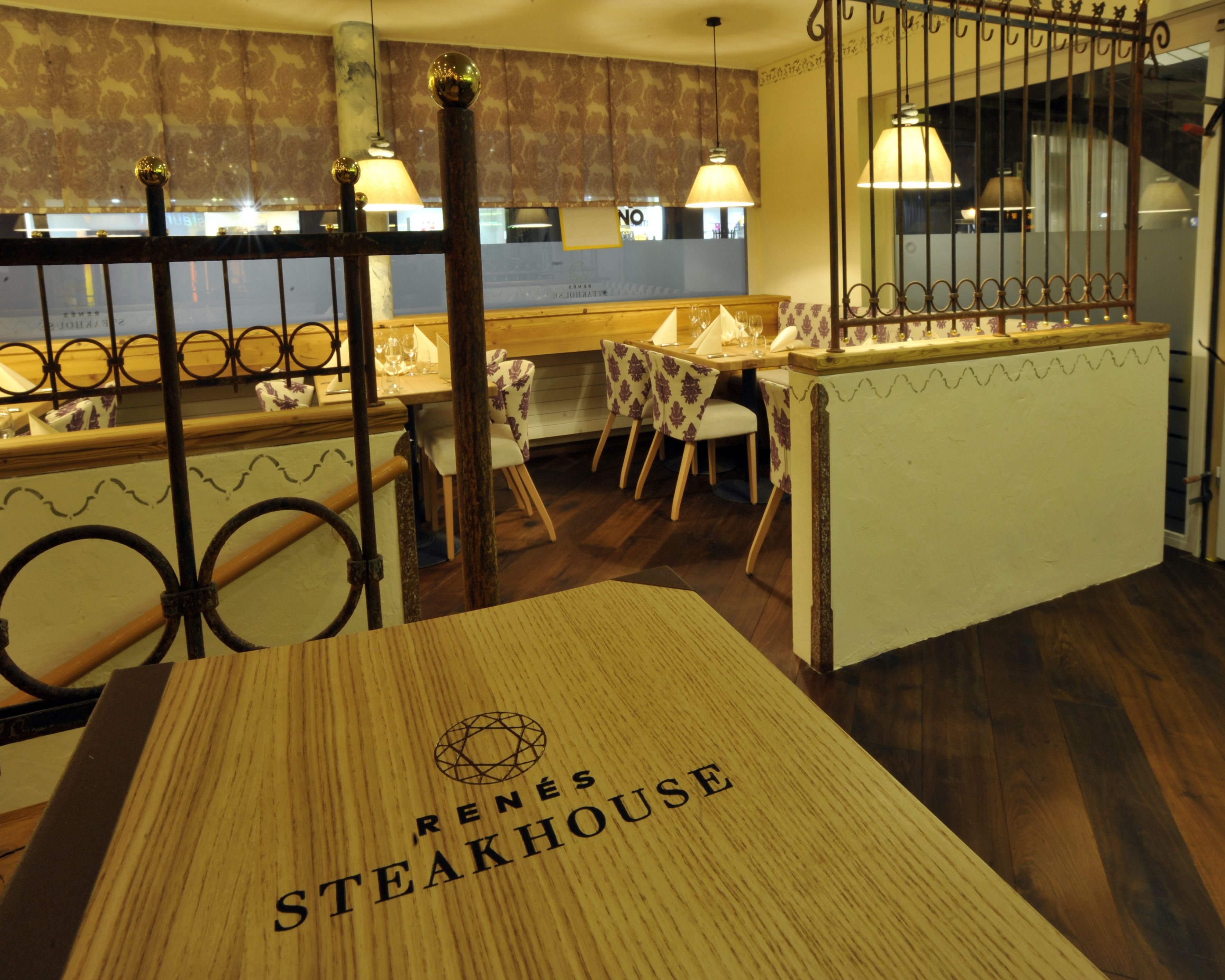 A restaurant interior with a wooden table labeled 'Renes Steakhouse', a bar area, and patterned chairs.