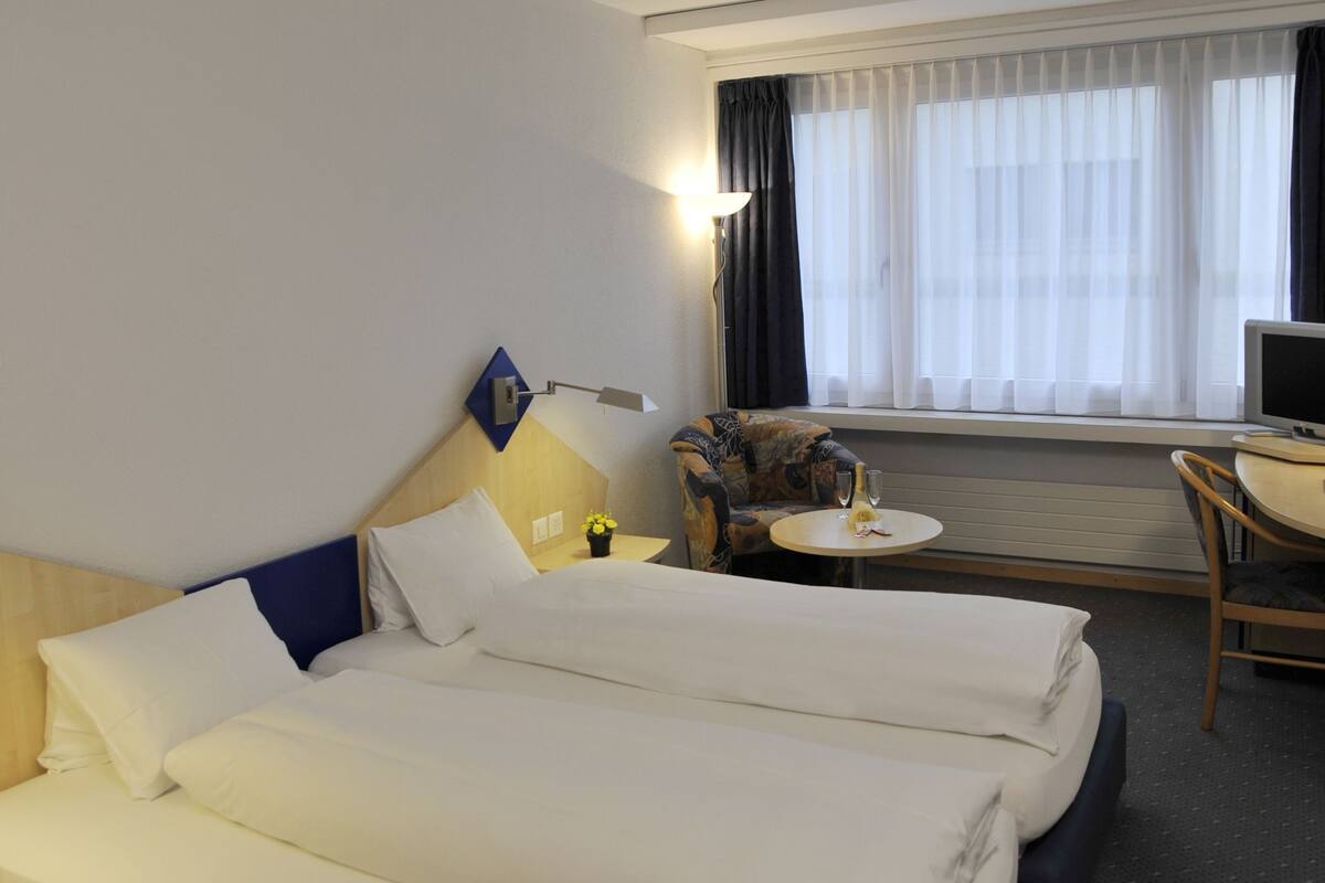 A hotel room with a double bed, a small round table, a chair, and a TV.