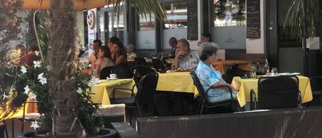 Un área de estar al aire libre con mesas y sillas, una palmera y un letrero que indica 'René's Steakhouse'.