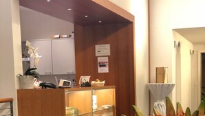 Aula, jossa on puinen vastaanottotiski, lasivitriini ja maljakko täynnä oransseja kukkia.