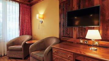A hotel room with a wooden desk, two striped armchairs, a flat-screen TV, and a lamp.
