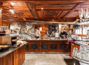 A rustic interior with wooden beams, a stone wall, and a buffet counter with various food items and glassware.