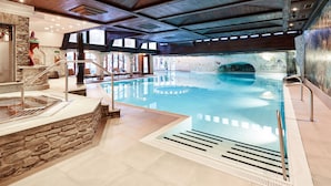 Una piscina interior con paredes de piedra, vigas de madera y una escalera de piedra que lleva a un área de hidromasaje.