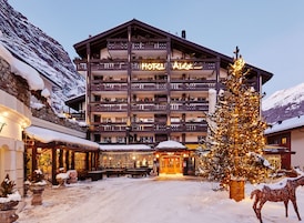Um hotel com vários andares, varandas, um pinheiro de Natal e paisagem coberta de neve.