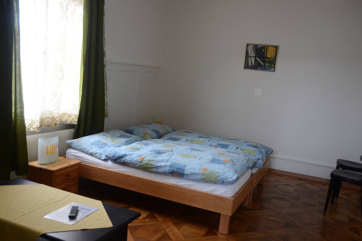 A room with a bed, a nightstand, a chair, and a window with curtains.