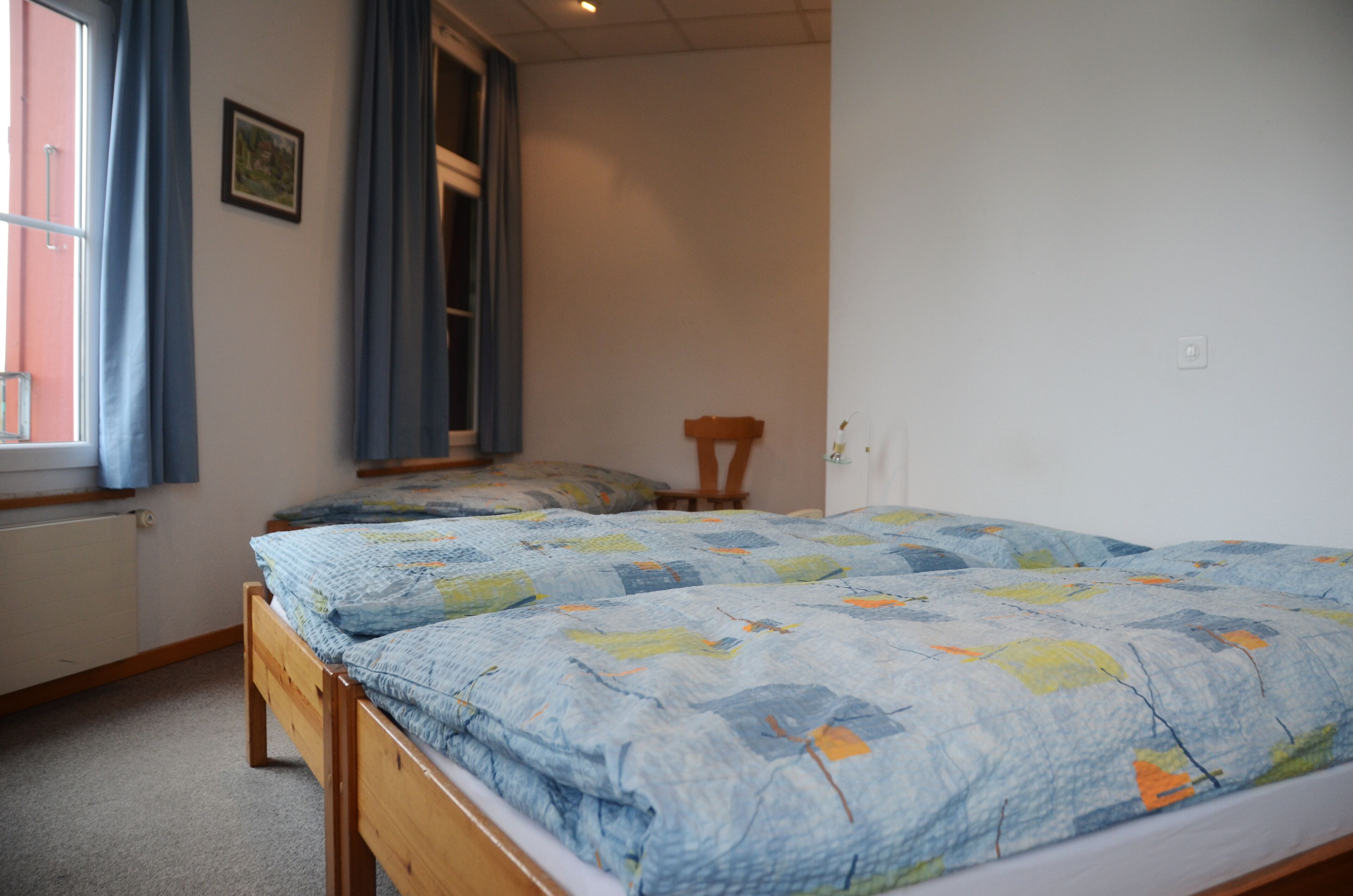 Een slaapkamer met een houten bed, een raam met gordijnen, een radiator en een deur.