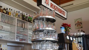 A bar area with a multi-tiered glass display and a sign reading "RUGENBRÄU". - Hotel Bahnhof (Schupfen)