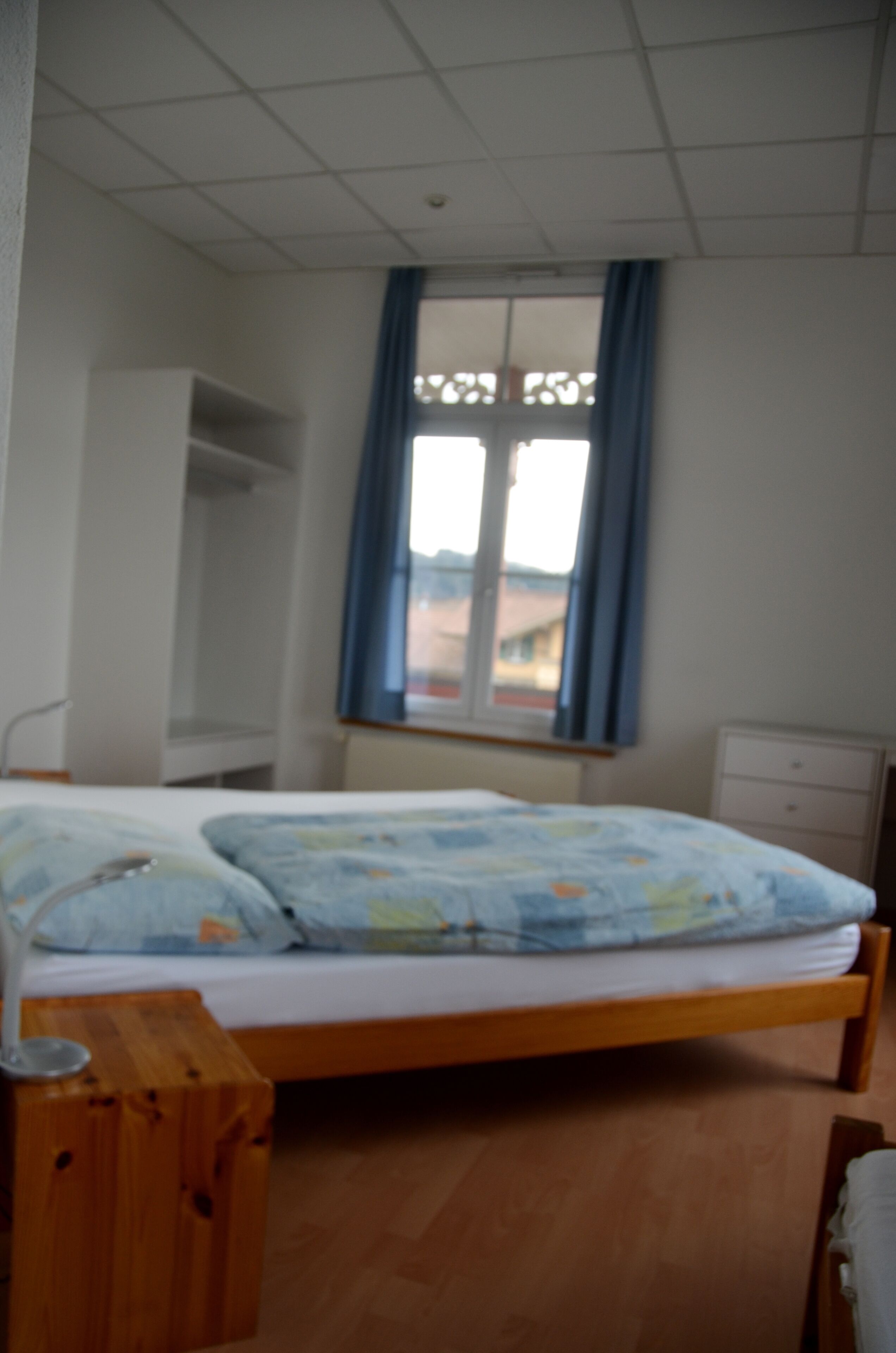 Un dormitorio con una cama, mesita de noche de madera y una ventana con cortinas.