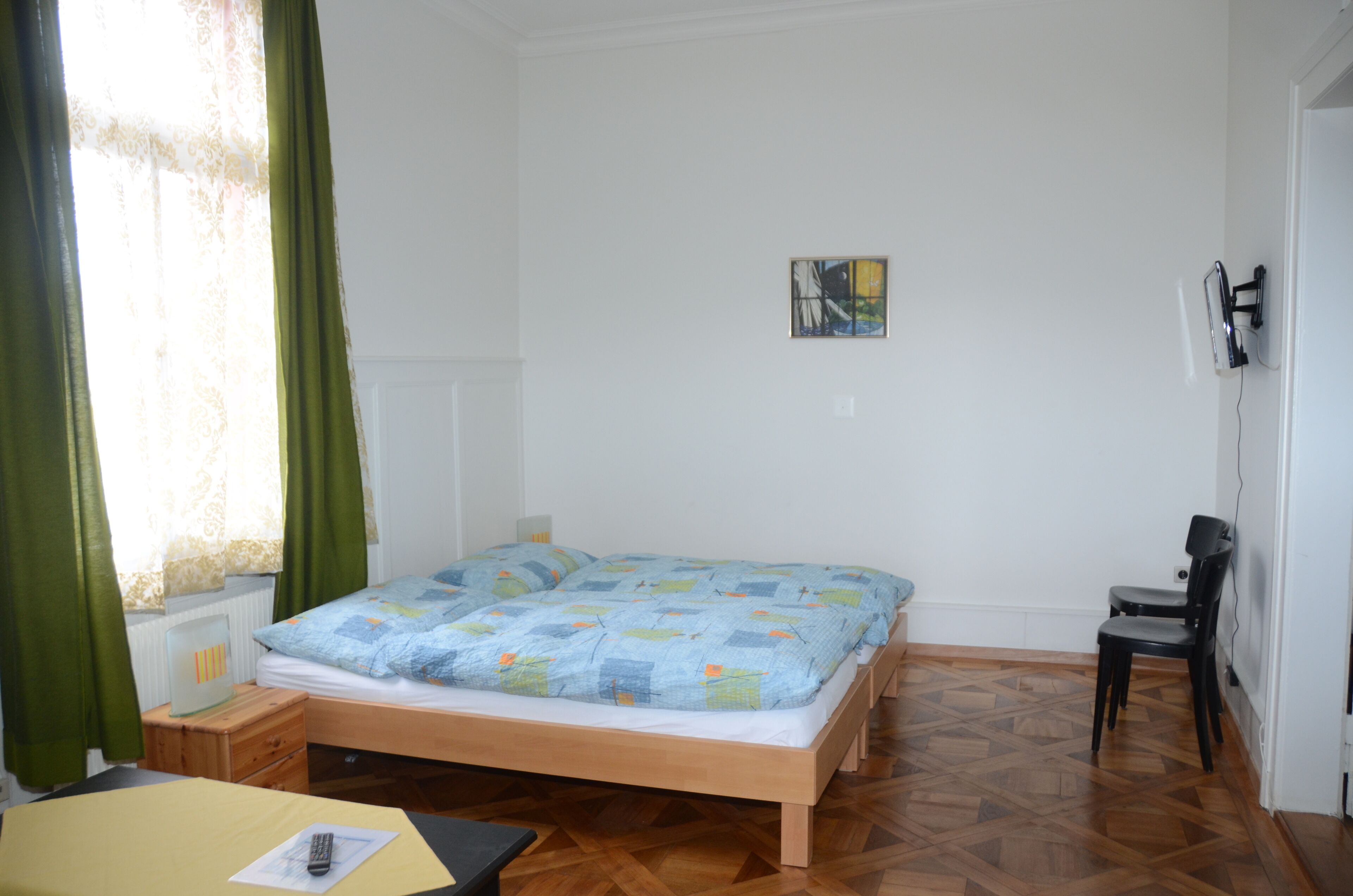 Un dormitorio con cama de madera, un escritorio con silla, un radiador y una ventana con cortinas.