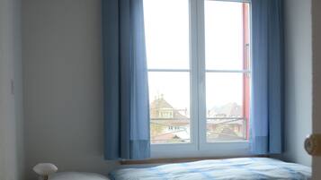 A single bed with a wooden frame, a bedside table with a lamp, and a window with blue curtains.
