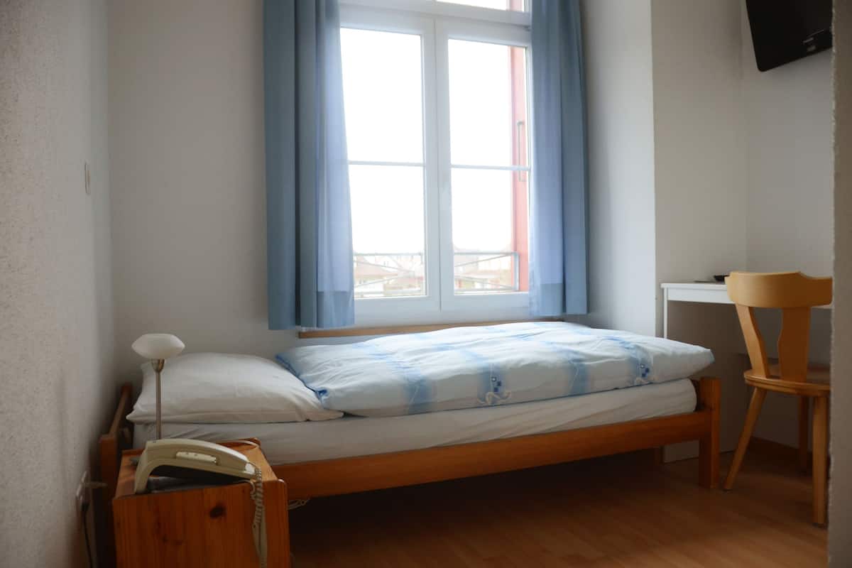 A small, single-bed room with a wooden bed, a desk, and a chair.