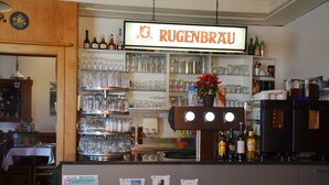 A bar area with shelves of glasses and bottles, a coffee machine, and a sign reading "RUGENBRAU". - Hotel Bahnhof (Schupfen)