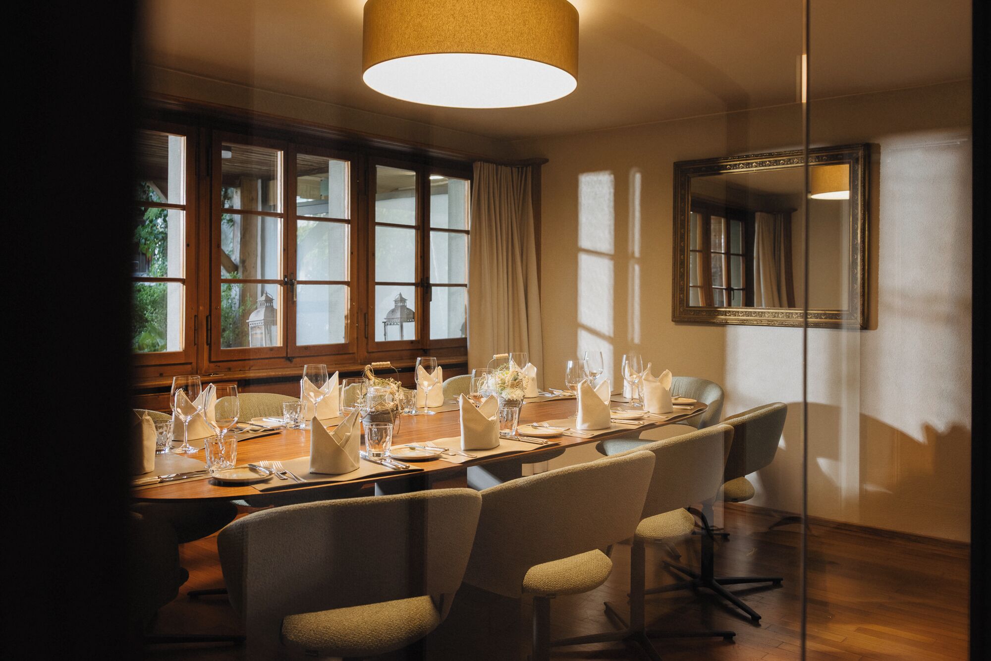 A conference room with a long table set for a meeting, large windows, and a mirror on the wall.