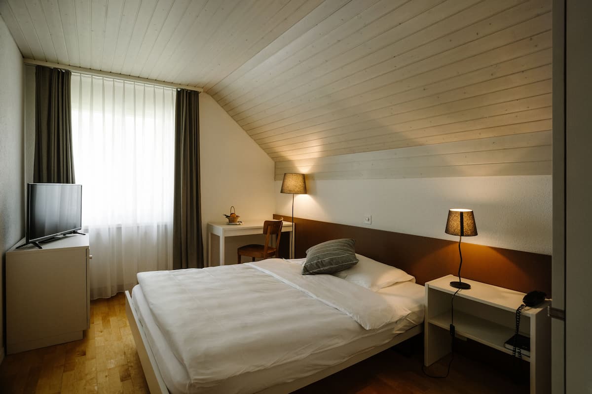 A hotel room with a bed, a desk, a chair, a TV, and two bedside lamps.
