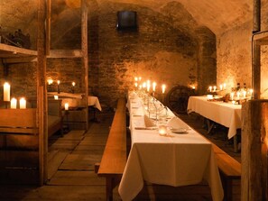 A long table set for dining in a rustic stone-walled room with candles.