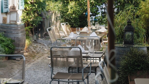 An outdoor dining area with metal chairs and tables, surrounded by greenery and decorative lanterns. - Bäre Madis (Madiswil)