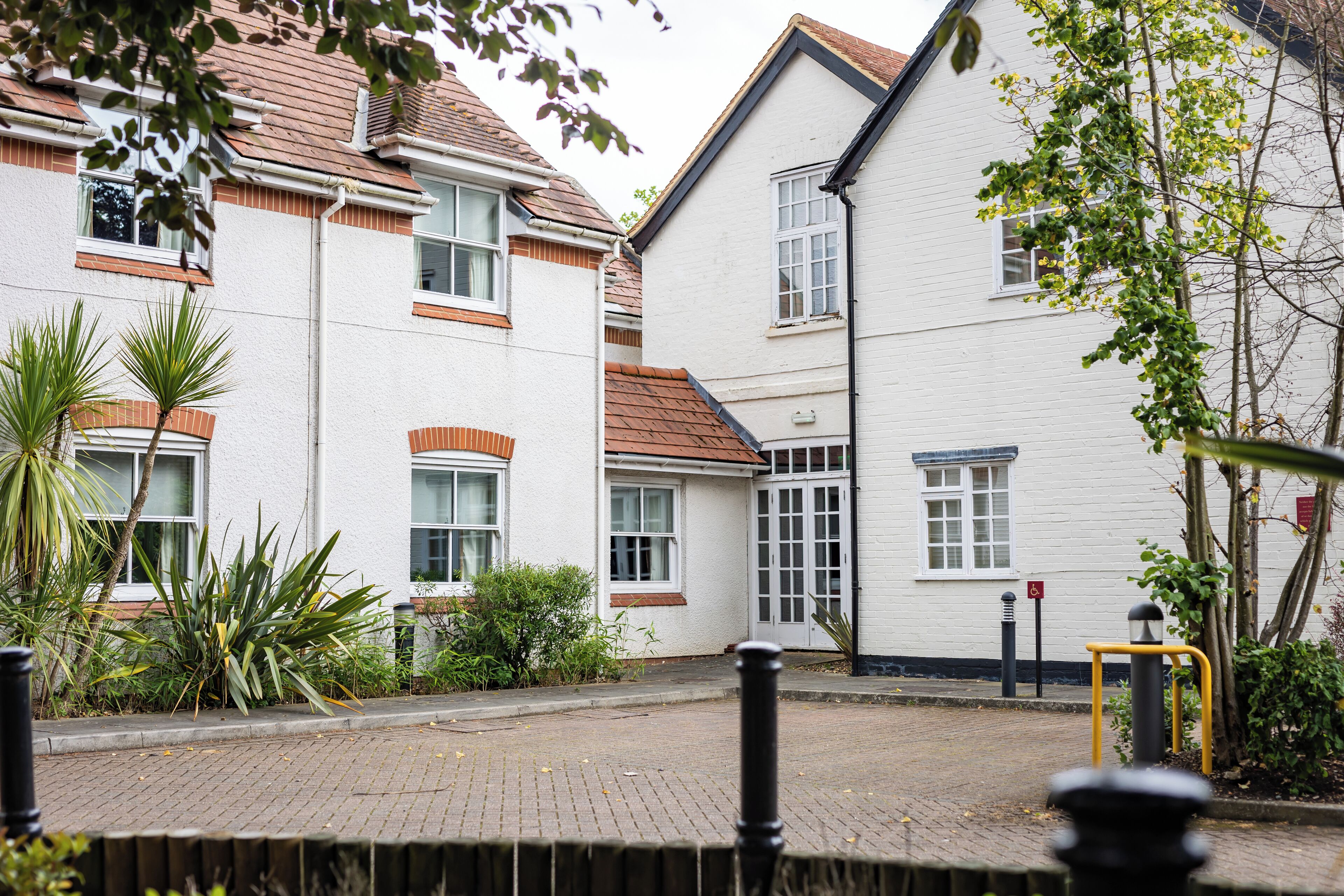 A residential building with a brick pathway, white walls, and multiple windows.