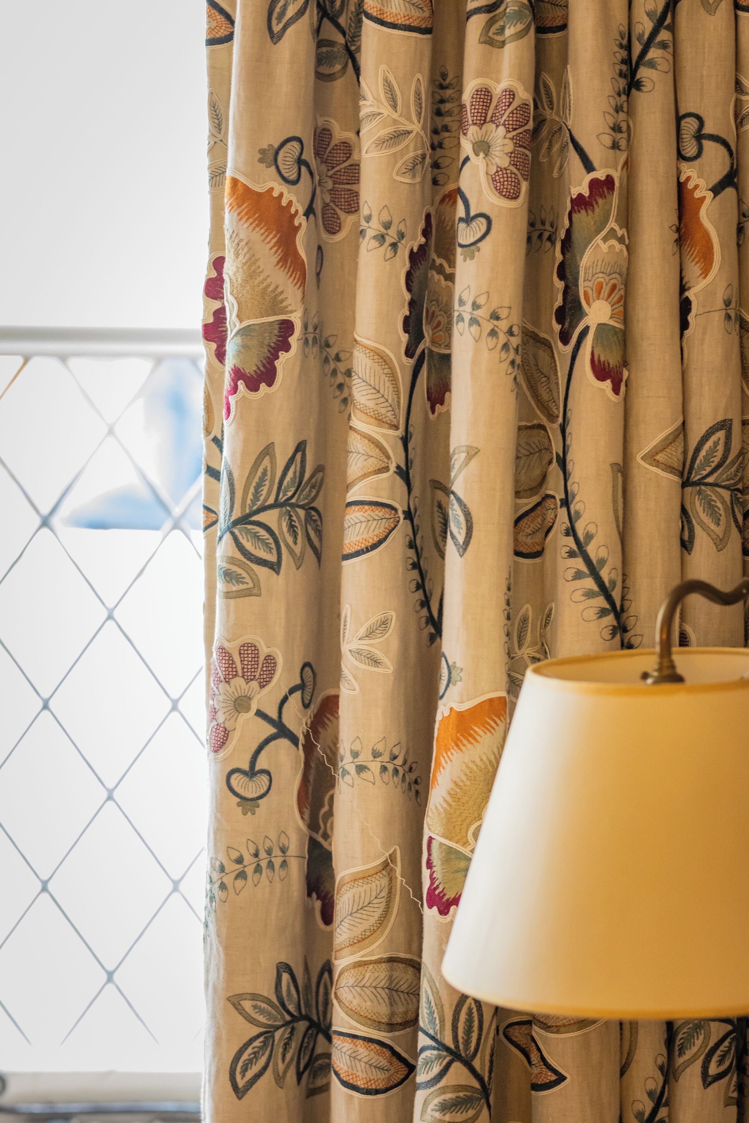 A window with a curtain featuring a floral pattern and a lamp on a table.