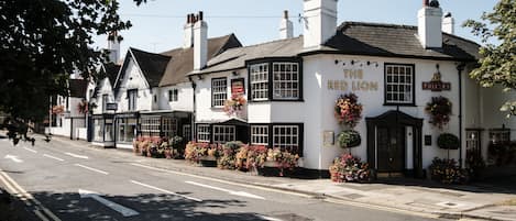 A traditional pub named 'The Red Lion' with a classic white facade, multiple chimneys, and flower boxes.