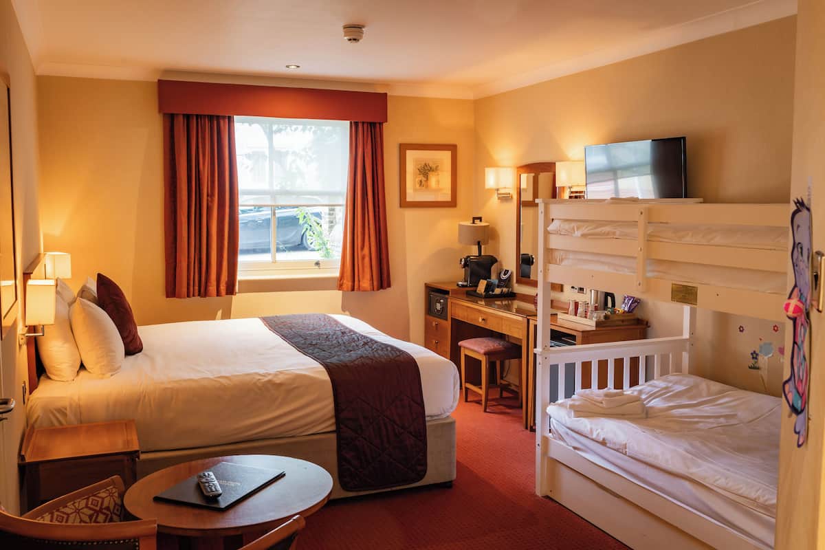 A hotel room with a large bed, a desk, a computer, a TV, and a bunk bed.