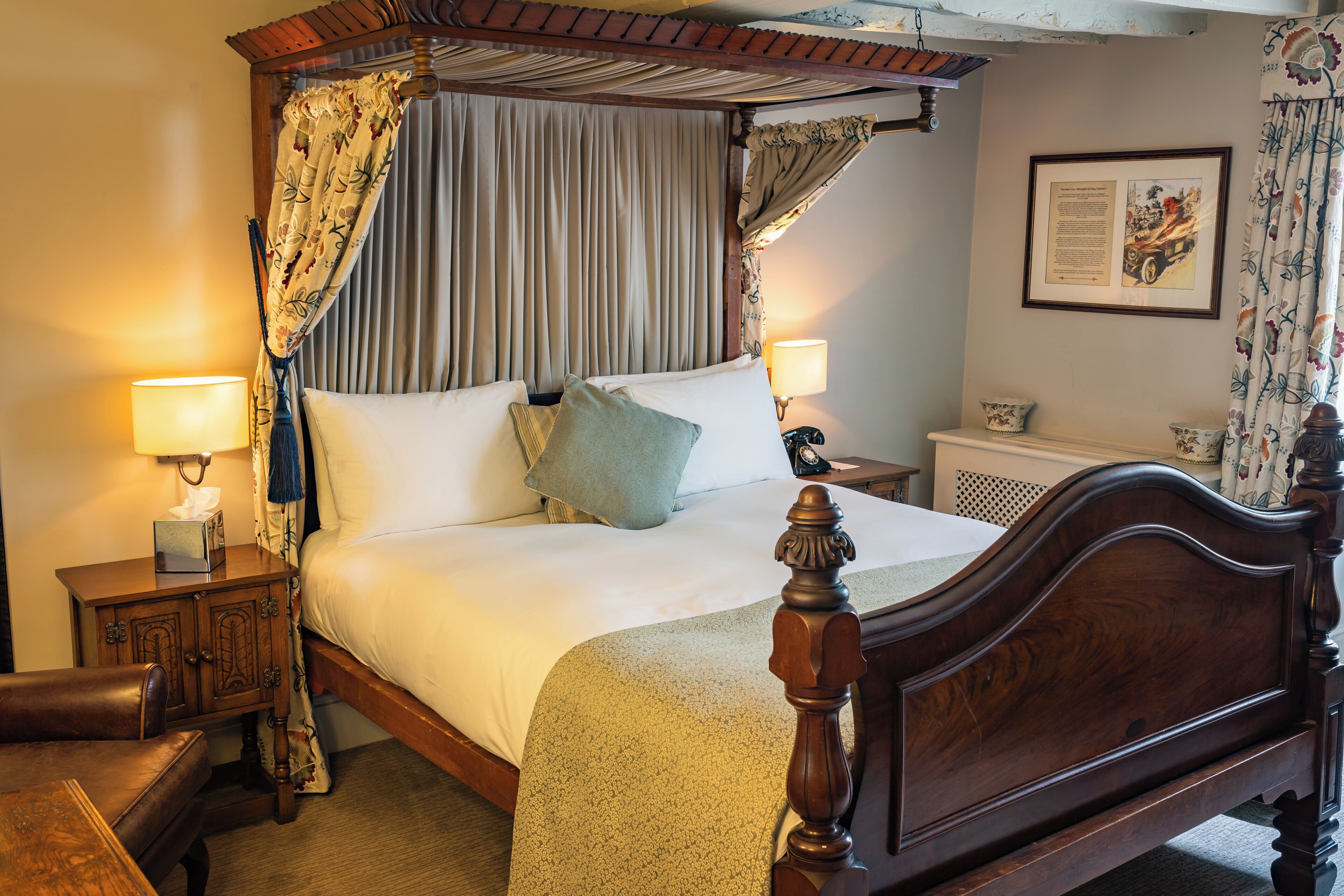A four-poster canopy bed with a wooden headboard, two bedside tables with lamps, and a framed picture on the wall.