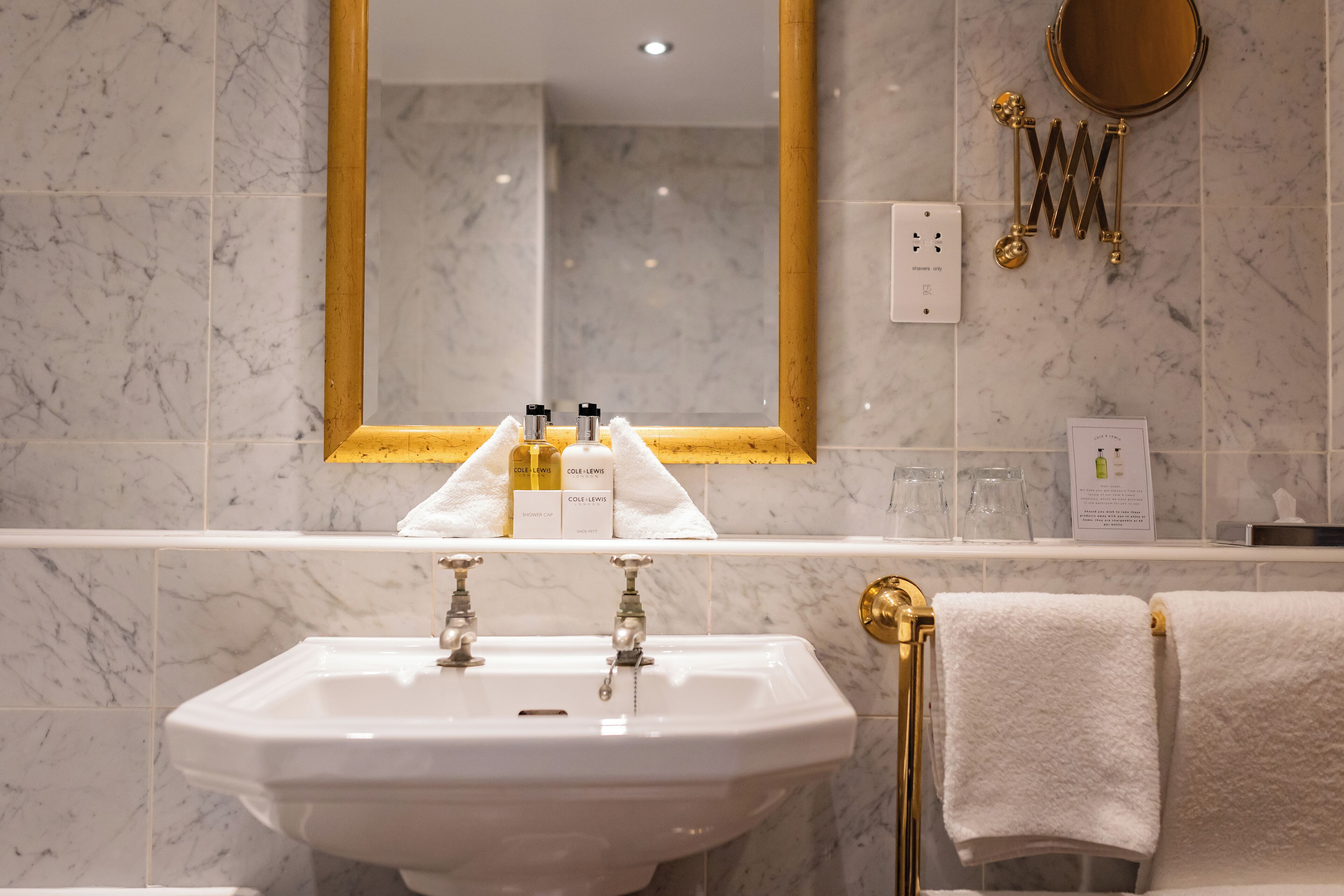 A bathroom with a white sink, gold fixtures, a large mirror with a gold frame, and a towel rack with towels.