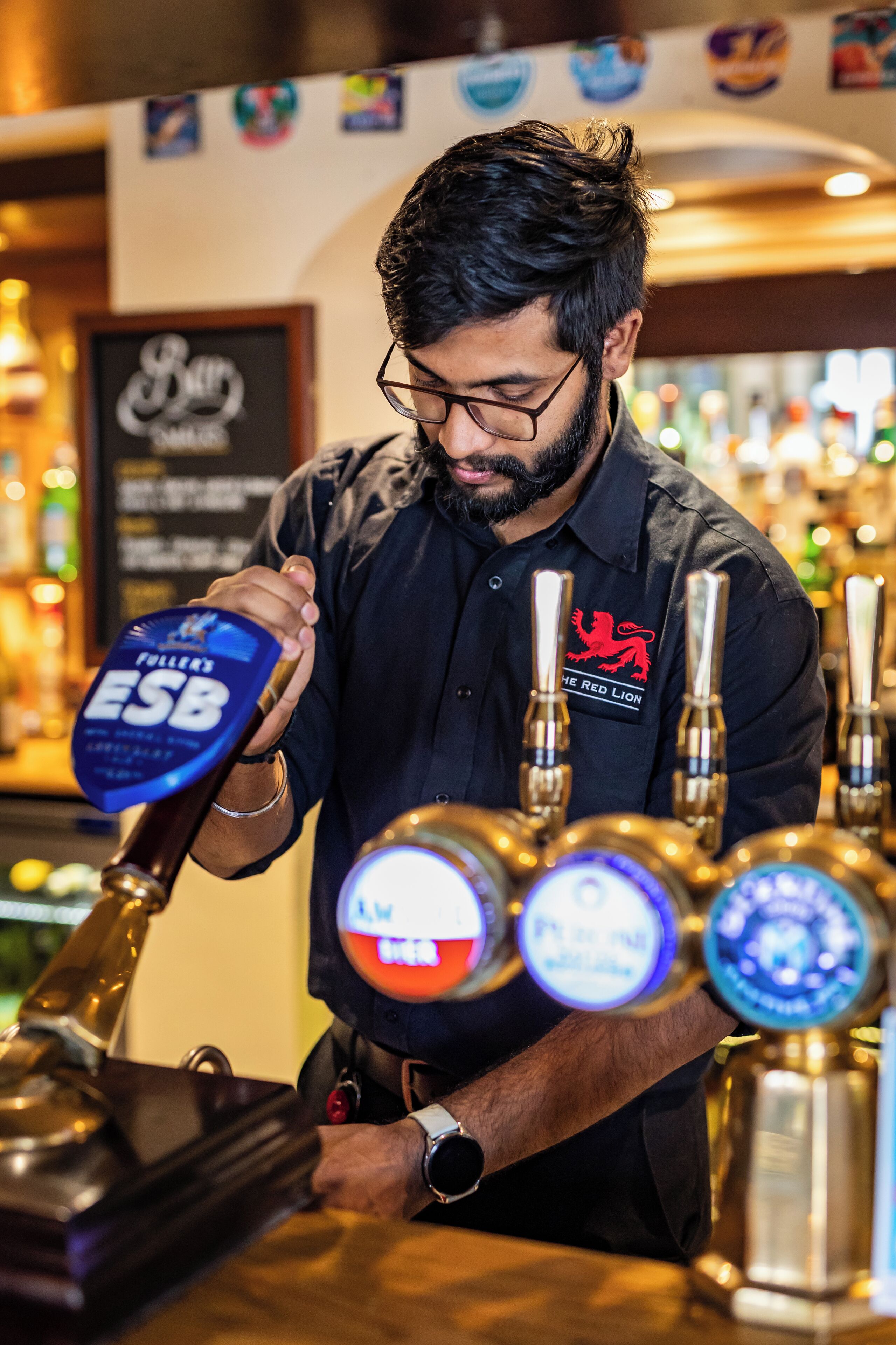 A bartender pouring beer from a tap labeled "ESB" in a bar setting.