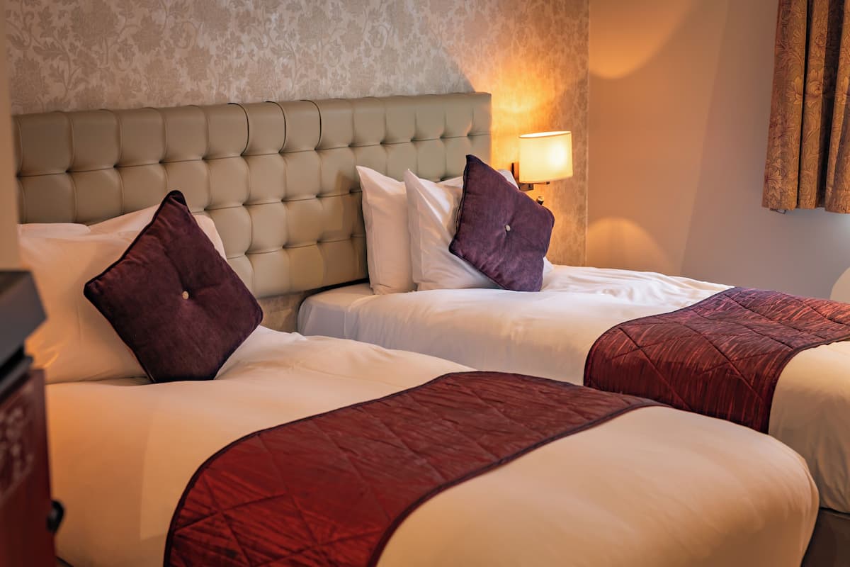 Two beds with headboards, a wall-mounted lamp, and a patterned wallpaper.