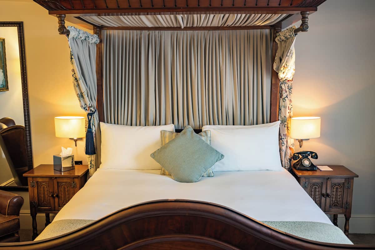 A four-poster bed with a canopy, two bedside lamps, a telephone, and a nightstand with a tissue box.