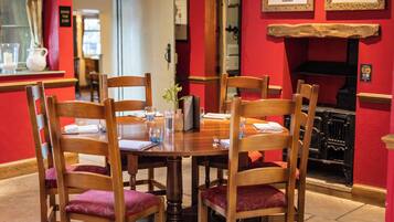 A dining area with a wooden table and chairs, a vase with flowers, and a red wall with framed pictures.