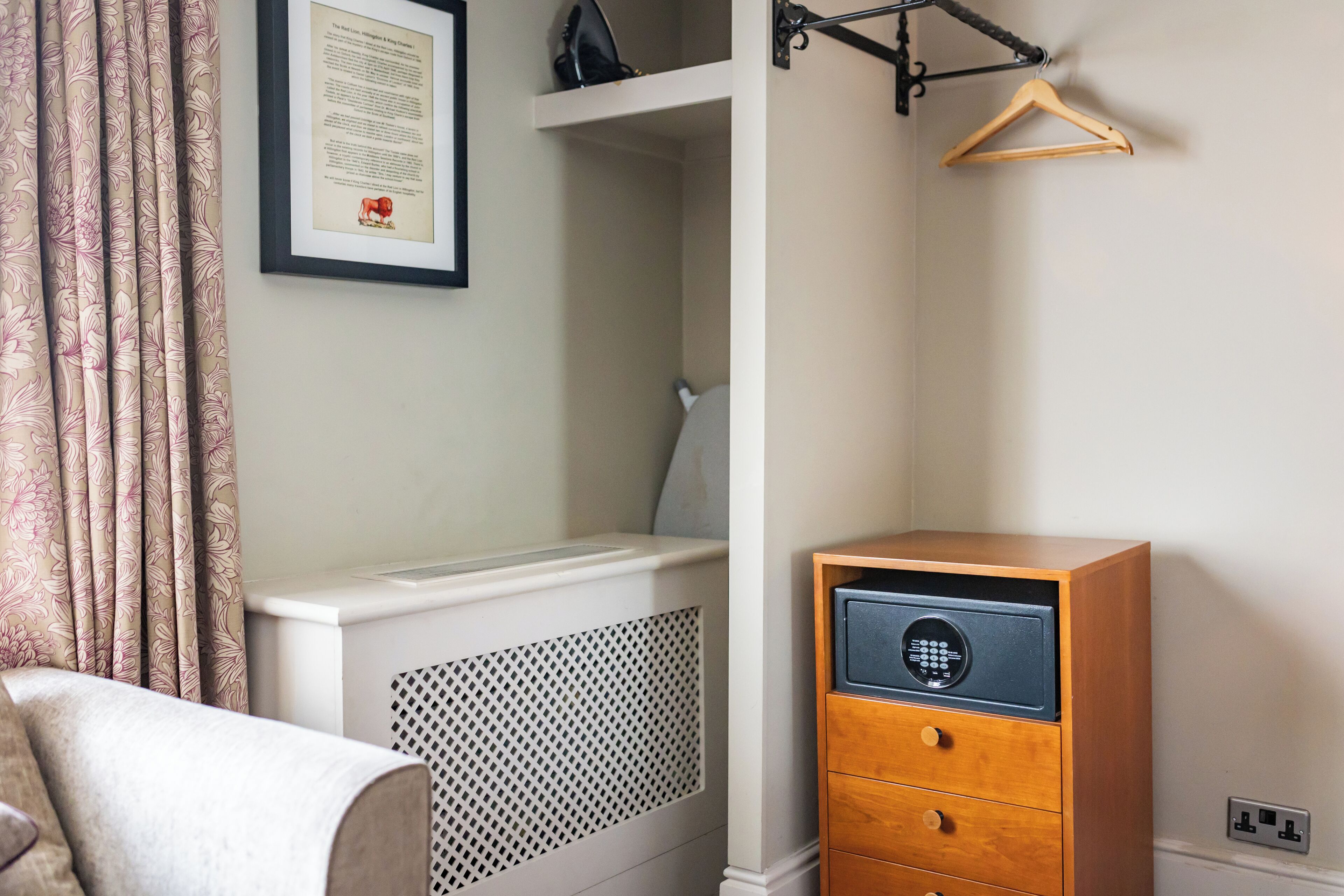 A bedroom with a bed, a dresser, a hanging coat rack, and a framed certificate on the wall.