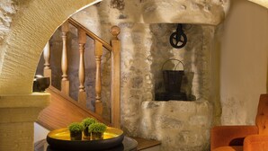 A stone-walled room with a wooden staircase, a small table with a bowl and plants, and an orange chair. - Les Tournelles (Paris)