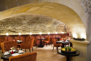 Un ristorante con pareti in pietra, sedie rivestite in arancione e tavoli con piatti e bicchieri bianchi.