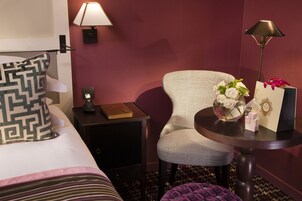 A hotel room with a bed, a nightstand, a chair, a table, and a lamp.