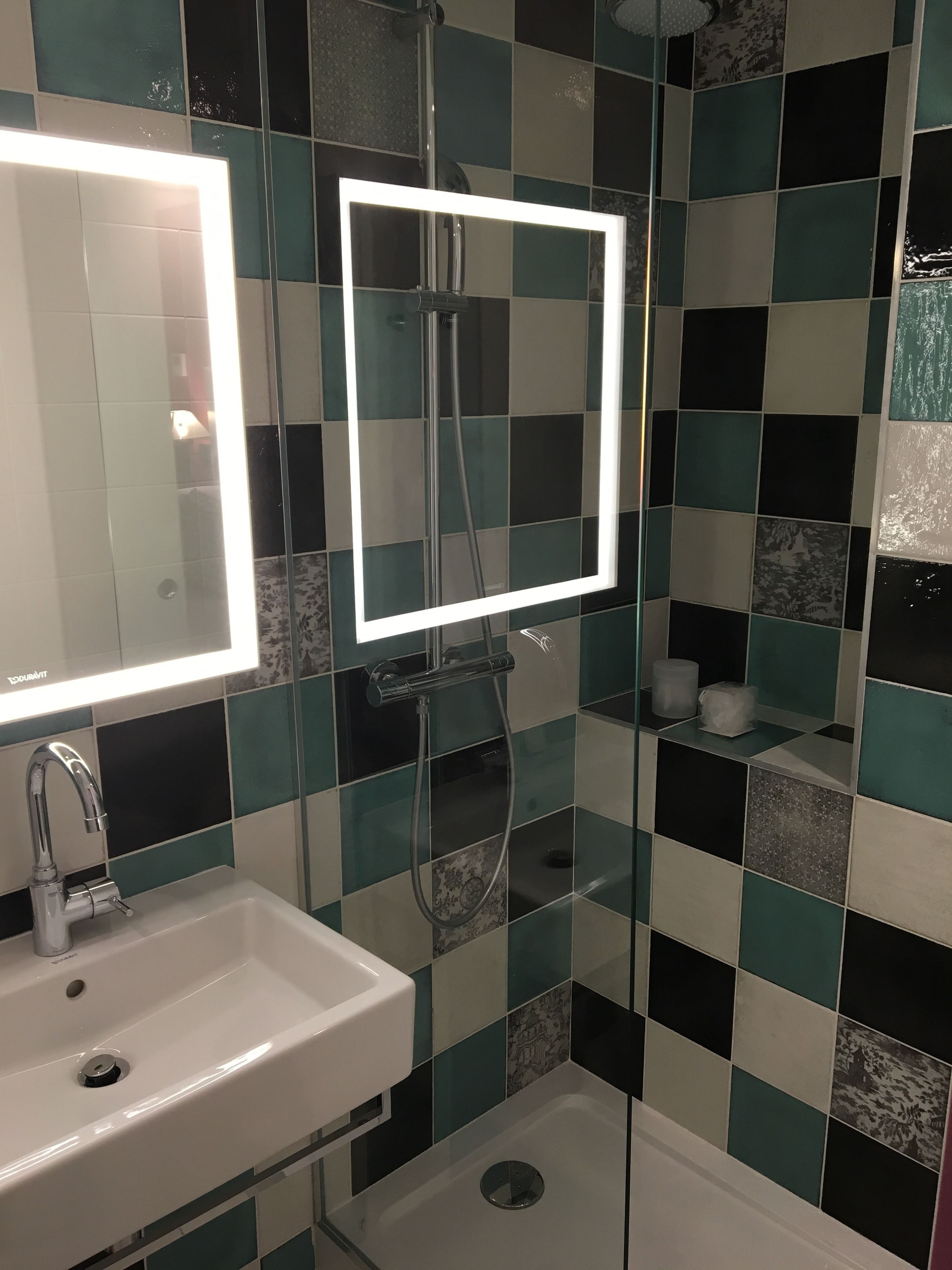 Une salle de bain avec un lavabo blanc, un miroir avec un éclairage intégré et un espace douche.