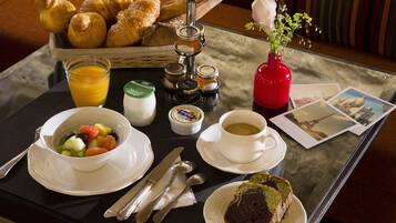 A breakfast table with croissants, fruit, jam, coffee, and a vase with flowers.
