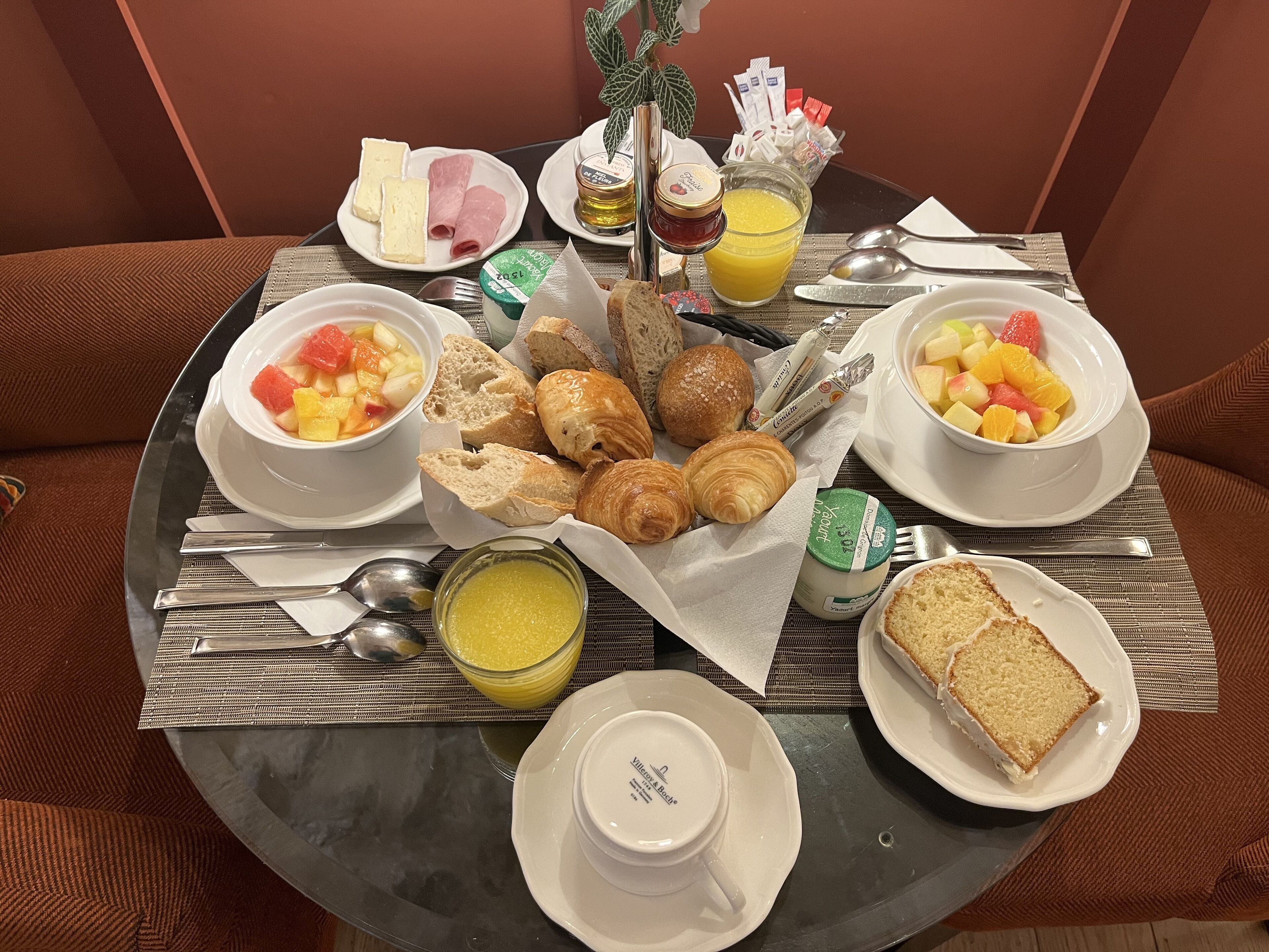 Een ontbijttafel met croissants, brood, fruit, kaas en toevoegingen.
