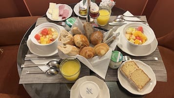 Een ontbijttafel met croissants, brood, fruit, kaas en toevoegingen.