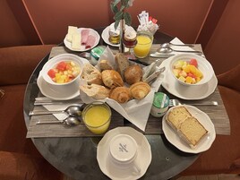 Ein Frühstückstisch mit Croissants, Brot, Obst, Käse und Beilagen.
