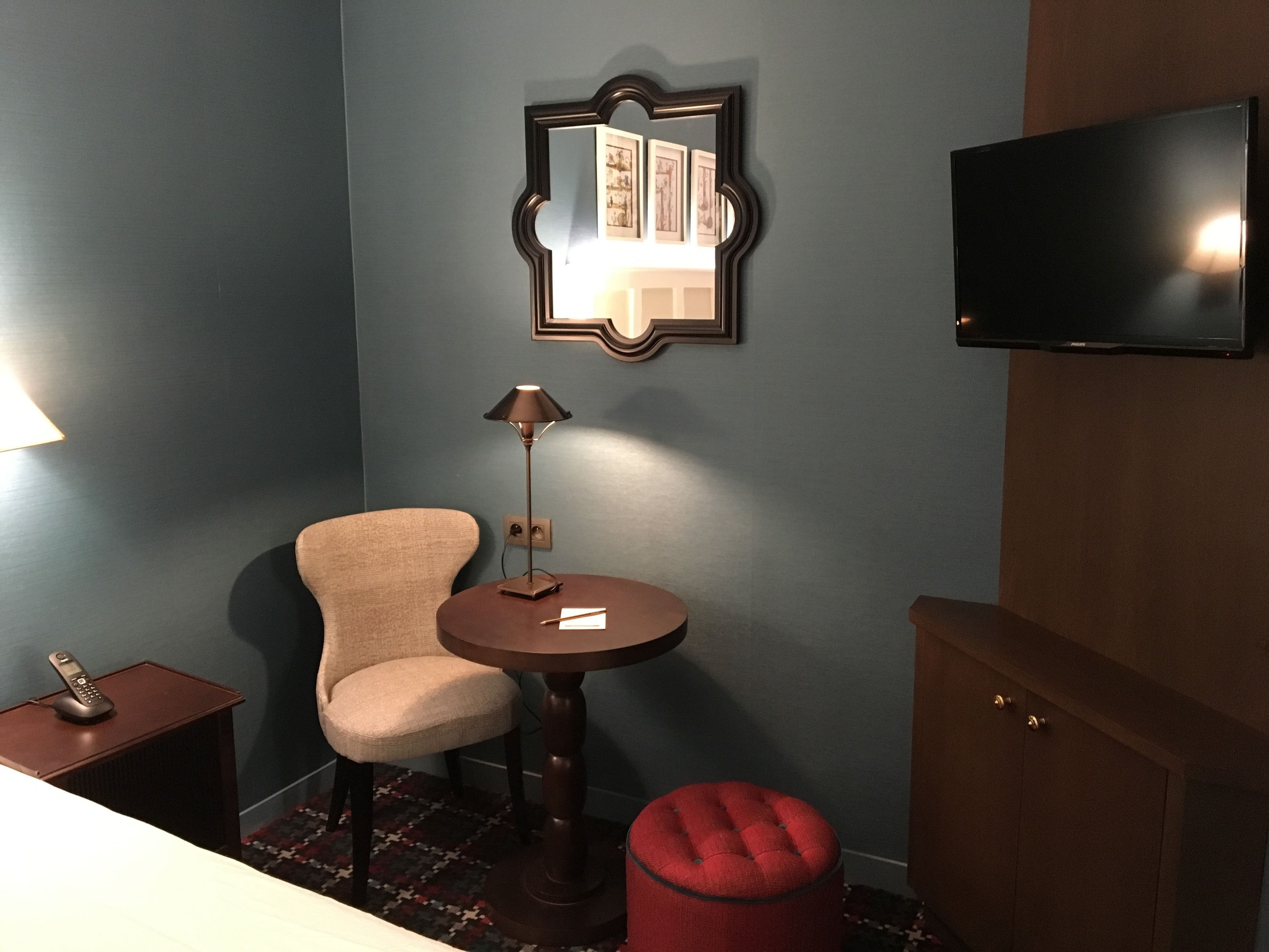 Une chambre d’hôtel avec un mur bleu, une armoire en bois, un téléviseur, une chaise, une petite table avec une lampe et un téléphone sur une table d’appoint.