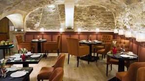 A restaurant with stone walls, round tables, and orange chairs. - Les Tournelles (Paris)