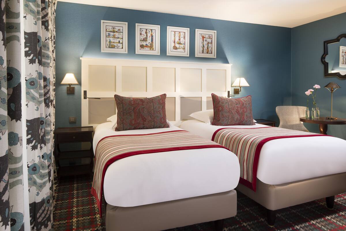 A hotel room with two beds, a headboard, a nightstand, a chair, a lamp, and a mirror.