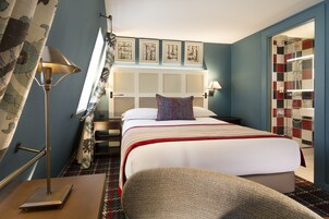 A hotel room with a bed, a nightstand, a lamp, a chair, and a shower area.